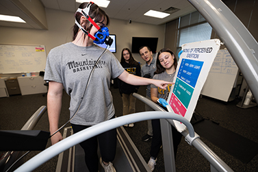 Person points to a chart that shows different levels of exertion based on colors while three people look on