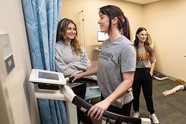 Woman stands on a scale with a meter in front of her while two people look on